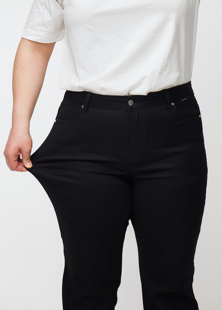 Schwarze Mid-Rise-Bootcut-Jeans in der Farbe Ravens. Ein Plus-Size-Model zieht am Jeansstoff am Oberschenkel, um den Stretch zu zeigen.
