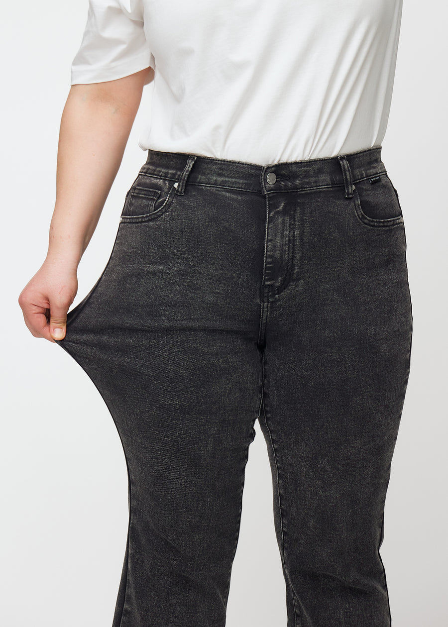 Dunkelgraue Mid-Rise-Bootcut-Jeans in der Farbe Shadows. Ein Plus-Size-Model zieht am Jeansstoff am Oberschenkel, um den Stretch zu zeigen.