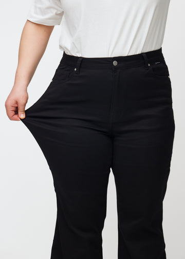 Das Plus-Size-Model zieht die Jeans am Oberschenkel, um den Stretch zu zeigen.