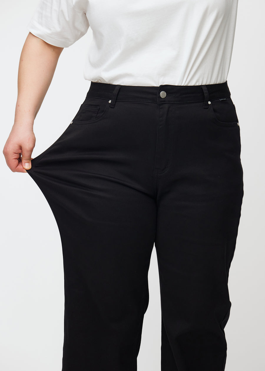 Das Plus-Size-Model zieht die Jeans am Oberschenkel, um den Stretch zu zeigen.