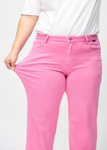 Loose-Jeans für Damen in Hellrosa, Farbe Flamingos. Ein Plus-Size-Model dehnt den Jeansstoff am Oberschenkel, um den Stretch zu zeigen.