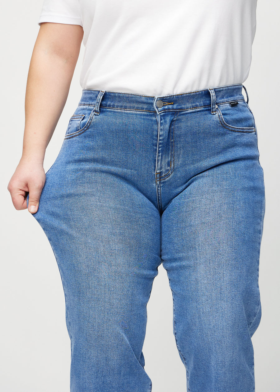 Das Plus-Size-Model zieht die Jeans am Oberschenkel, um den Stretch zu zeigen.