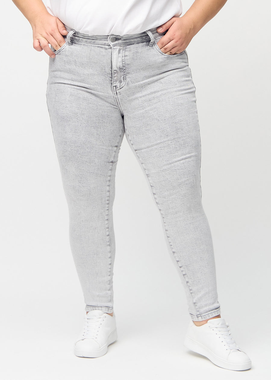 Hellgrauer Denim skinny jeans, Modellname Ashes, der an einem Plus-Size-Model eng am Bein anliegt, von vorne gesehen.