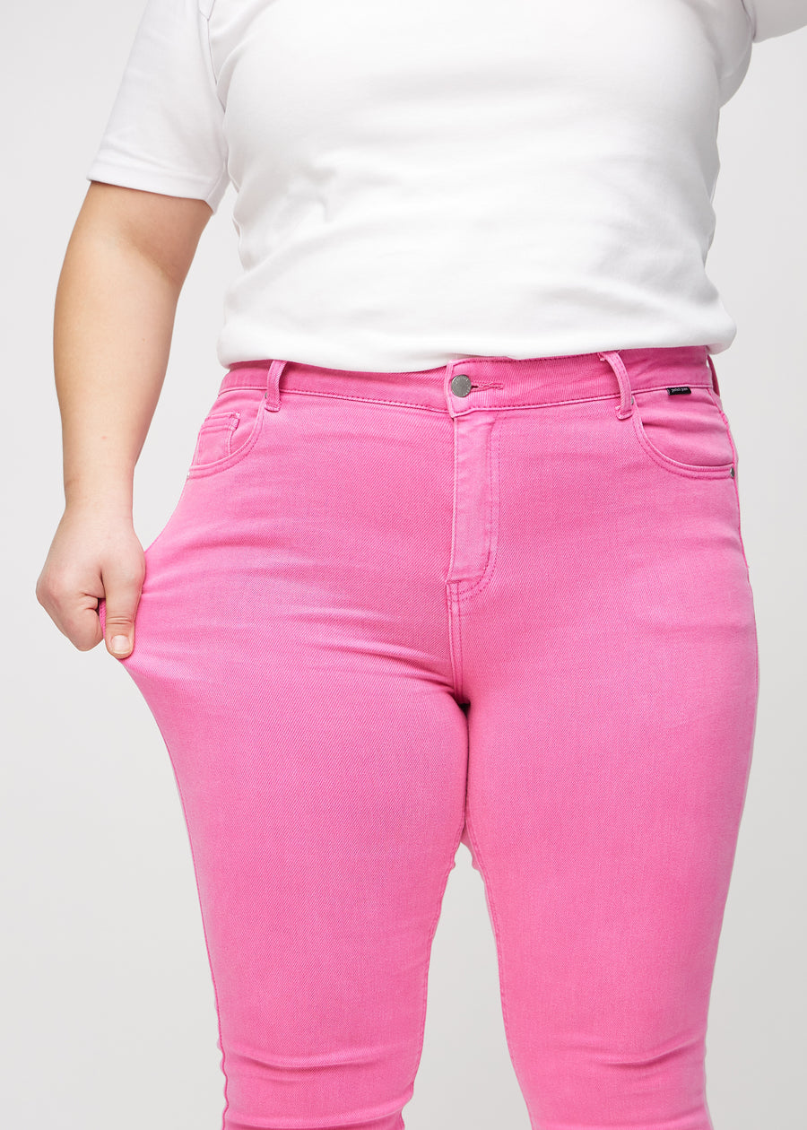 Skinny-Jeans für Damen in Hellrosa, Farbe Flamingos. Ein Plus-Size-Model dehnt den Jeansstoff am Oberschenkel, um den Stretch zu zeigen.