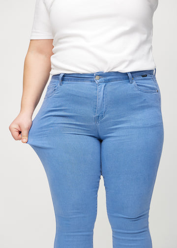 Skinny-Jeans für Damen in Blau, Farbe Geraniums. Ein Plus-Size-Model zieht am Jeansstoff am Oberschenkel, um den Stretch zu zeigen.