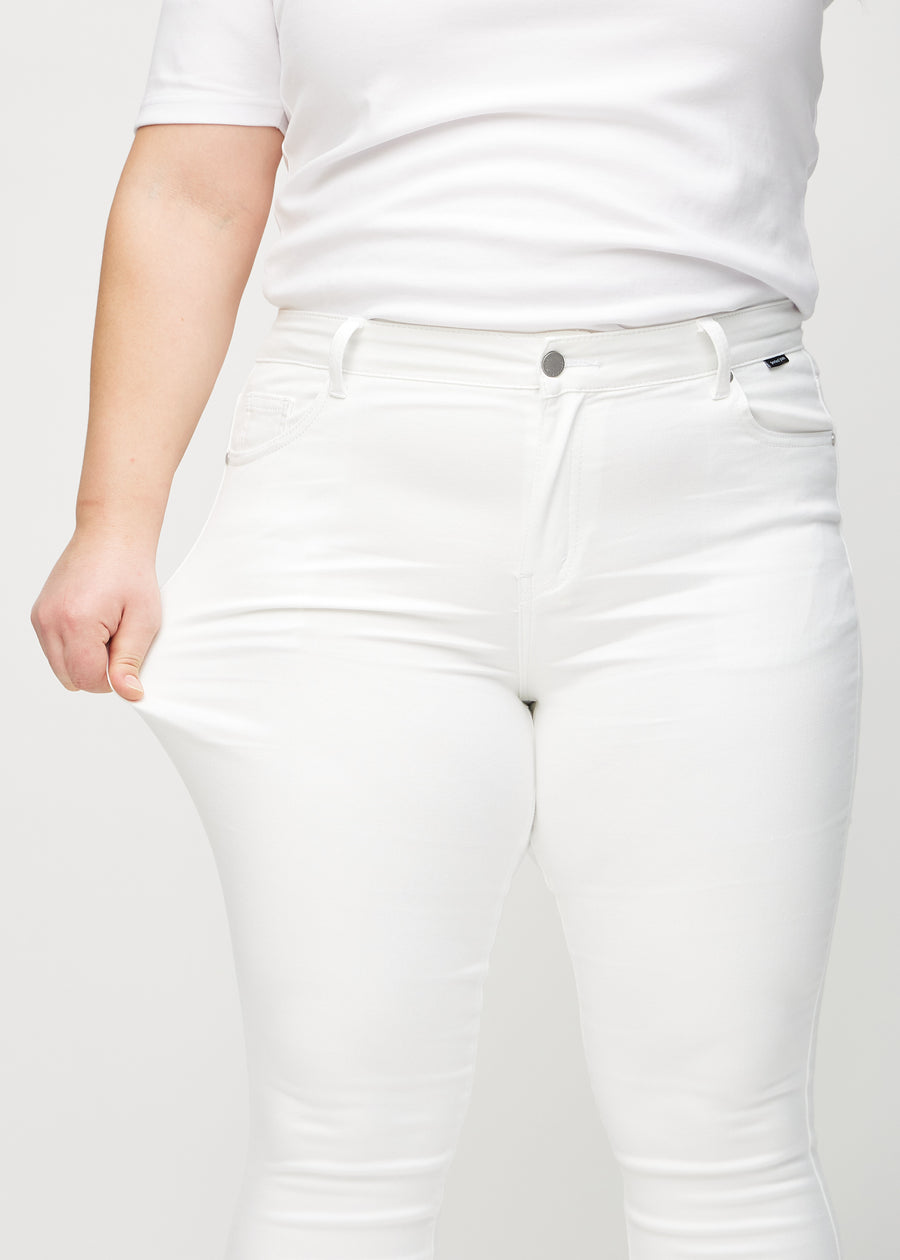 Skinny-Jeans für Damen in Weiß, Farbe Marguerites. Ein Plus-Size-Model dehnt den Jeansstoff am Oberschenkel, um den Stretch zu zeigen.