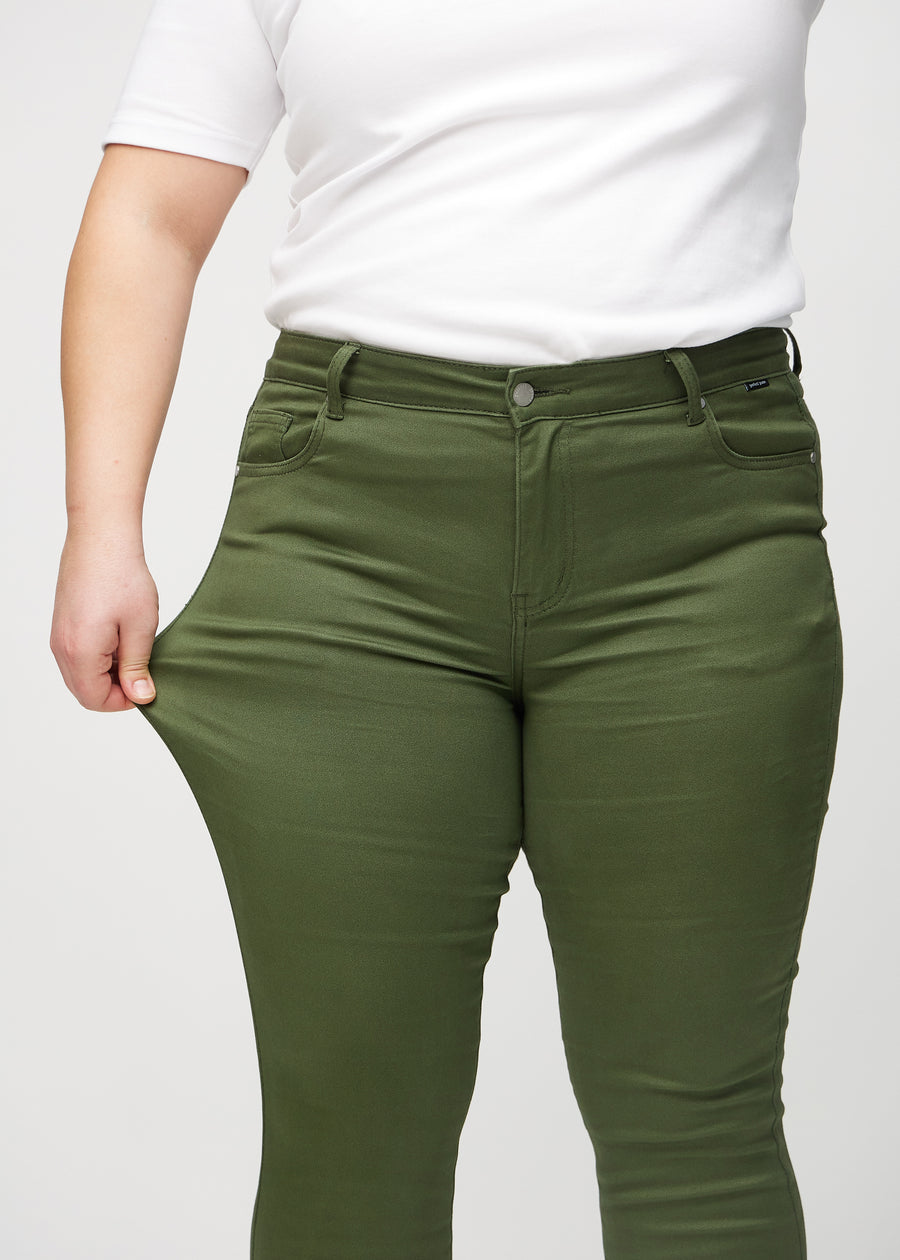 Skinny-Jeans für Damen in Dunkelgrün, Farbe Renewals. Ein Plus-Size-Model dehnt den Jeansstoff am Oberschenkel, um den Stretch zu zeigen.