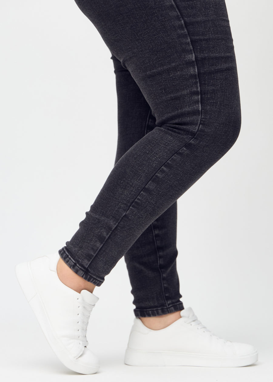 Skinny-Jeans für Damen in Dunkelgrau, Farbe Shadows. Nahaufnahme der eng anliegenden Beinabschlüsse am Knöchel eines Plus-Size-Models.