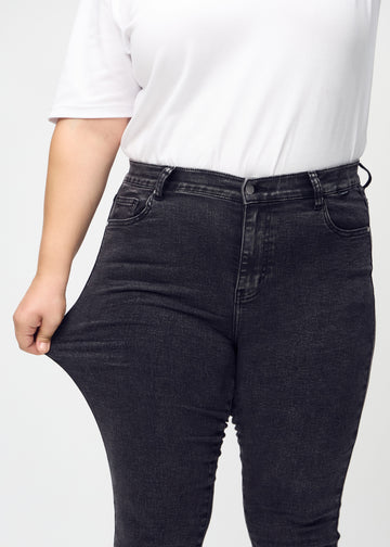 Skinny-Jeans für Damen in Dunkelgrau, Farbe Shadows. Ein Plus-Size-Model dehnt den Jeansstoff am Oberschenkel, um den Stretch zu zeigen.
