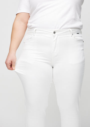 Slim-Jeans für Damen in Weiß, Farbe Marguerites. Ein Plus-Size-Model zieht am Jeansstoff am Oberschenkel, um den Stretch zu zeigen.