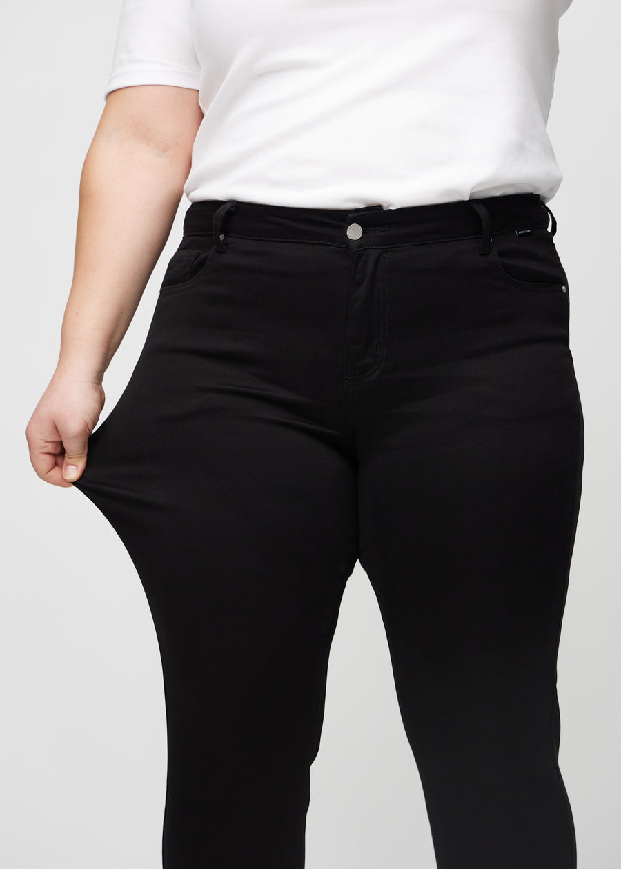 Slim-Jeans für Damen in Schwarz, Farbe Ravens. Ein Plus-Size-Model zieht am Jeansstoff am Oberschenkel, um den Stretch zu zeigen.