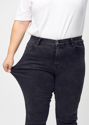 Ein Plus-Size-Model zieht die Jeans am Oberschenkel auseinander, um den Stretch zu zeigen.