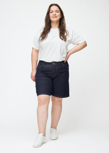 Ganzkörperbild eines Plus-Size-Models in tief dunkelblauen Denim-Shorts für Damen in der Farbe Midnights mit Loose-Passform.