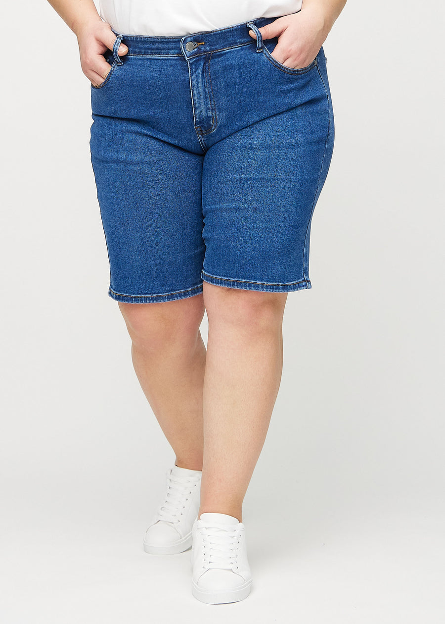 Dunkle Denim-regular middle shorts, Modellname Oceans, die gerade am Bein entlang fallen und knapp über dem Knie enden, an einem Plus-Size-Model von vorne gesehen.