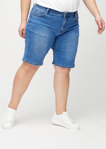Denim regular middle shorts, Modellname Rivers, die gerade am Bein entlang verlaufen und knapp über dem Knie enden, an einem Plus-Size-Model von vorn gesehen.