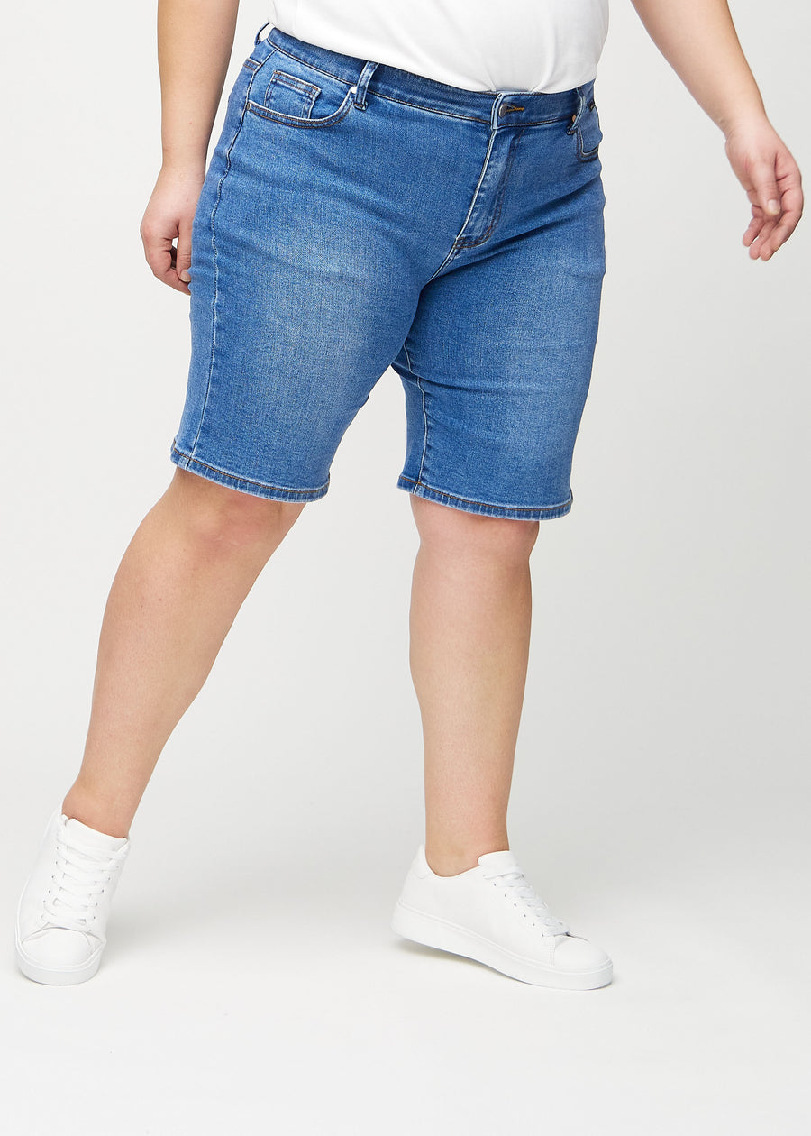 Denim regular middle shorts, Modellname Rivers, die gerade am Bein entlang verlaufen und knapp über dem Knie enden, an einem Plus-Size-Model von vorn gesehen.