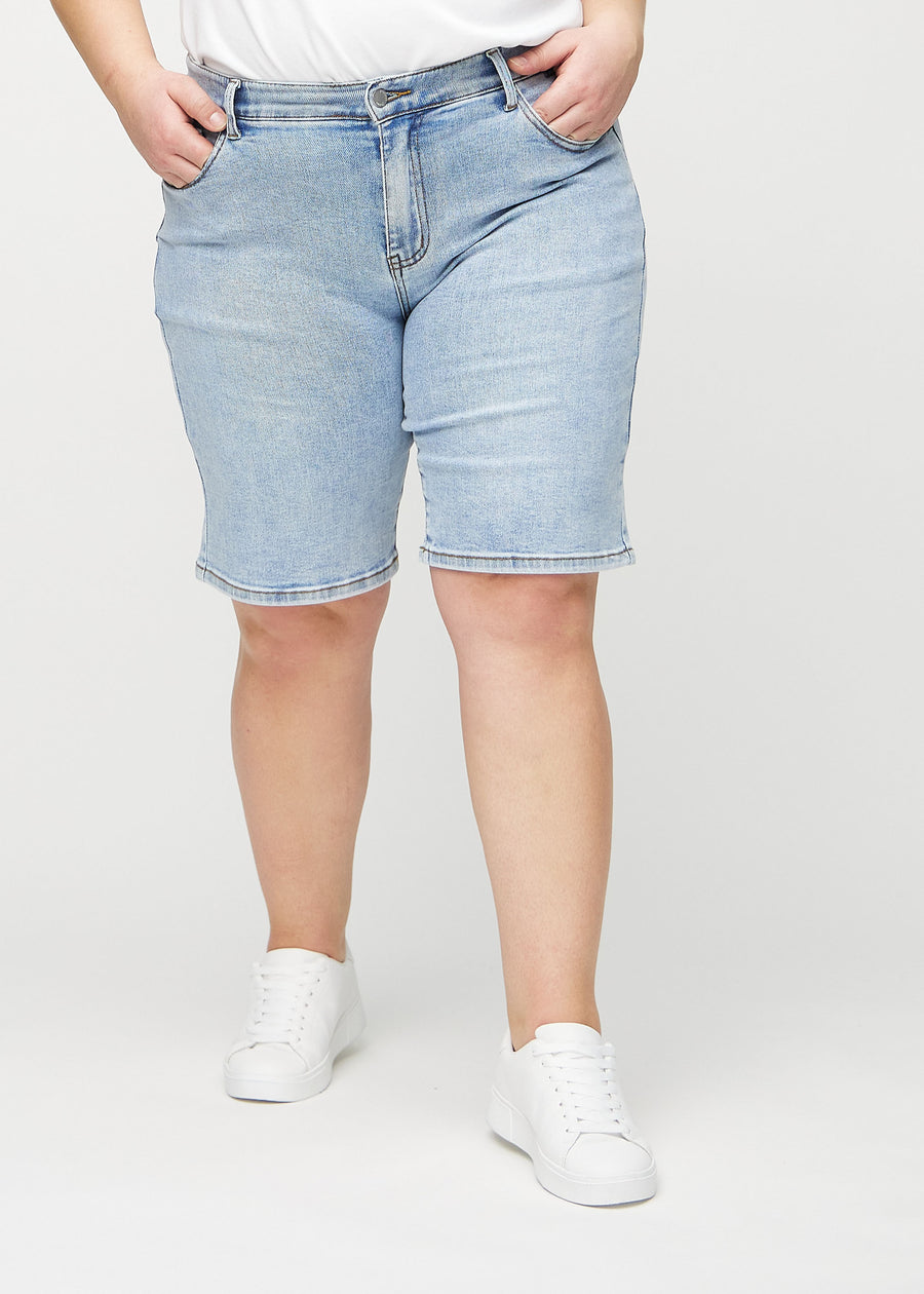 Hellblaue Denim-regular middle shorts, Modellname Waves, die am Bein gerade nach unten fallen und knapp über dem Knie enden, an einem Plus-Size-Model von vorne gesehen.