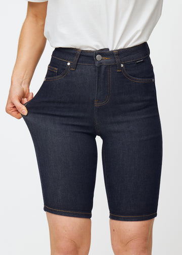 Model dehnt tief dunkelblaue Denim-Shorts für Damen in der Farbe Midnights am Oberschenkel, um den Stretch des Materials zu zeigen.