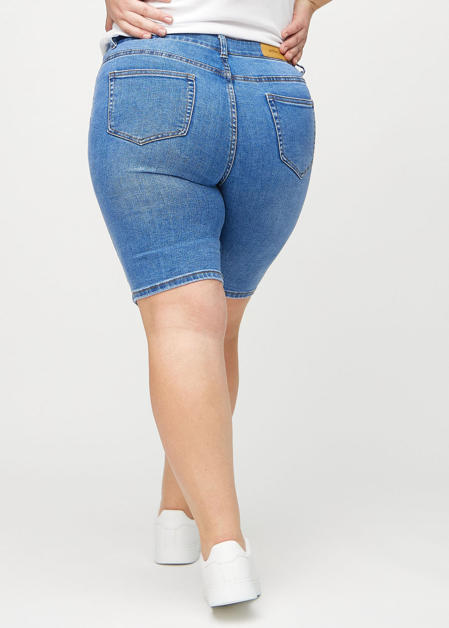 Denim skinny middle shorts von hinten an einem Plus-Size-Model gesehen, sodass man das ganze Produkt sehen kann.