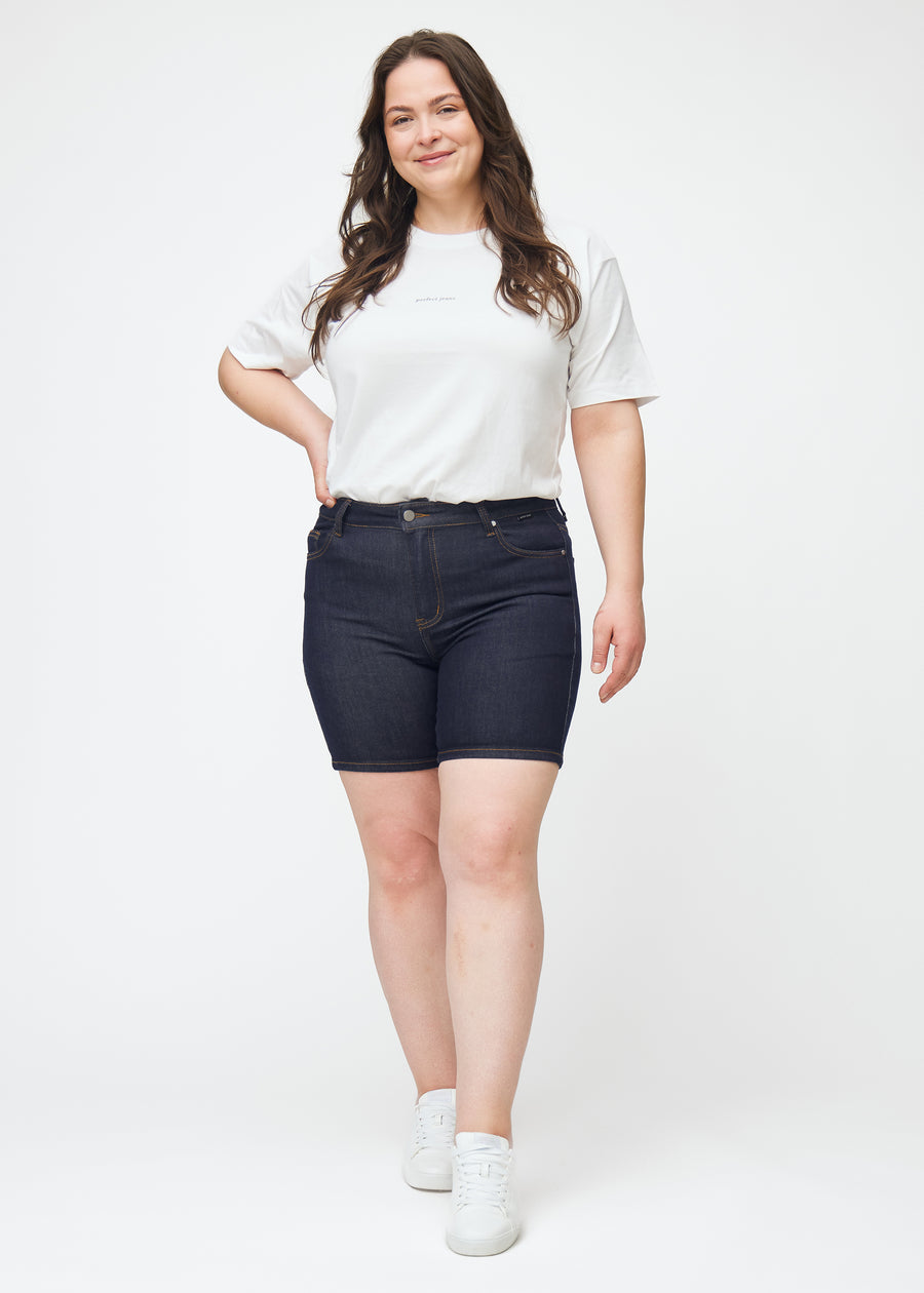 Ganzkörperbild eines Plus-Size-Models in tief dunkelblauen Denim-Shorts für Damen in der Farbe Midnights mit Skinny-Passform.