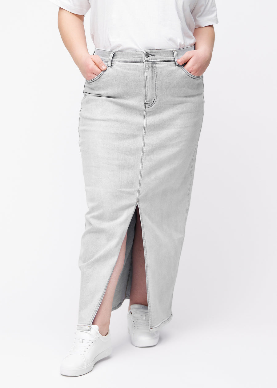 Langer hellgrauer Denimrock für Damen in der Farbe Ashes. Vorderansicht an einem Plus-Size-Model, der Rock fällt von der Hüfte gerade bis zum Knöchel und hat vorne einen Schlitz unterhalb des Knies.