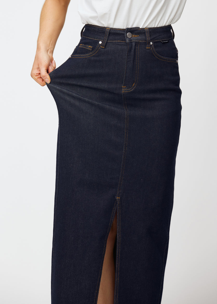 Model dehnt den langen tief dunkelblauen Denim-Rock für Damen in der Farbe Midnights an der Hüfte, um den Stretch des Materials zu zeigen.