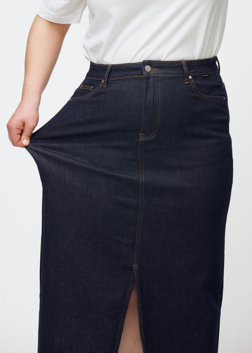 Plus-Size-Model dehnt den langen tief dunkelblauen Denim-Rock für Damen in der Farbe Midnights an der Hüfte, um den Stretch zu zeigen.