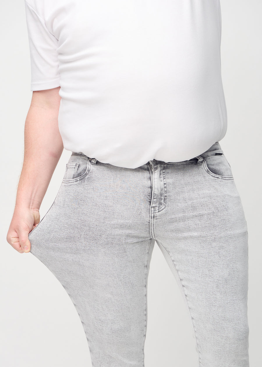 Ein Plus-Size-Model dehnt die Jeans am Oberschenkel, um den Stretch des Materials zu zeigen.