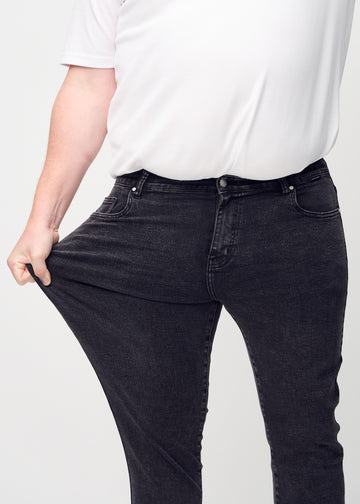Ein Plus-Size-Model dehnt die Jeans am Oberschenkel, um den Stretch des Materials zu zeigen.