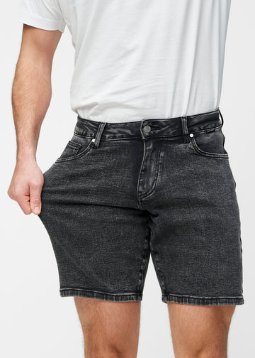 Modell dehnt dunkelgraue Denim-Shorts für Herren in der Farbe Shadows am Oberschenkel, um den Stretch des Materials zu zeigen.