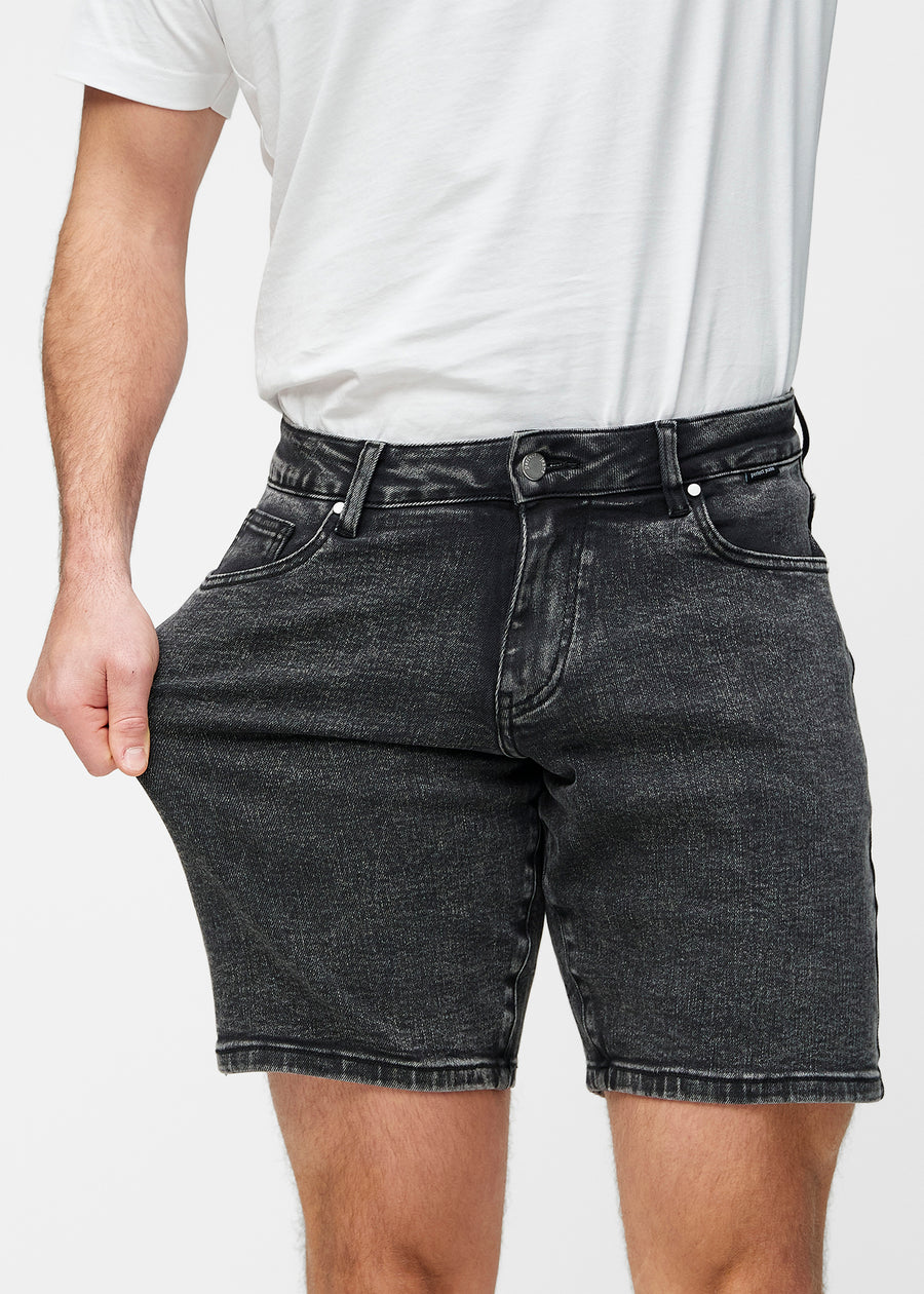 Modell dehnt dunkelgraue Denim-Shorts für Herren in der Farbe Shadows am Oberschenkel, um den Stretch des Materials zu zeigen.
