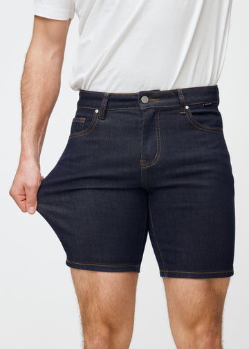 Model dehnt tief dunkelblaue Denim-Shorts für Herren in der Farbe Midnights am Oberschenkel, um den Stretch des Materials zu zeigen.