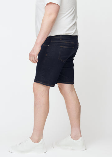 Tief dunkelblaue Denim-Shorts für Herren in der Farbe Midnights mit Slim-Passform, von der Seite auf einem Plus-Size-Model gesehen.
