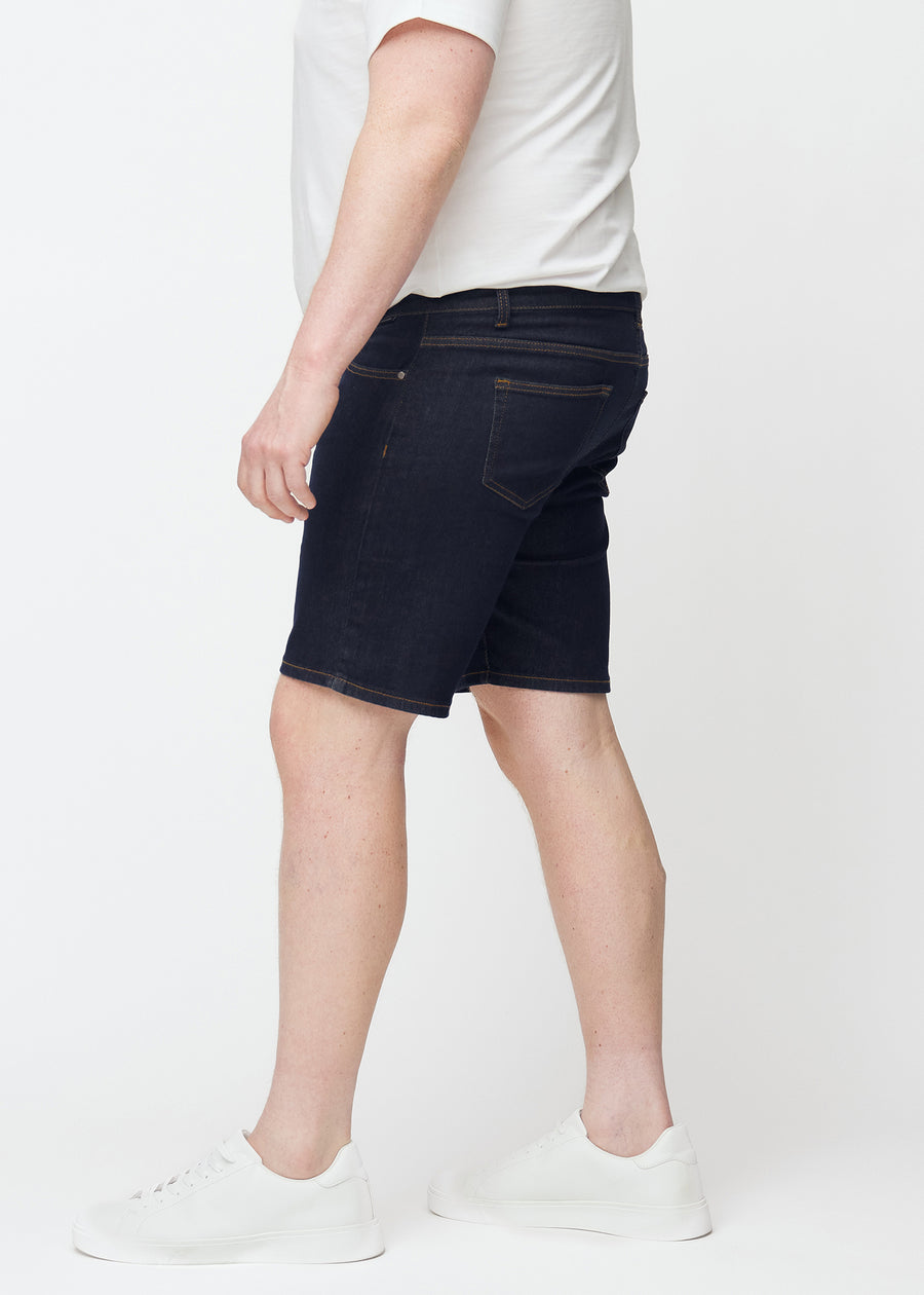 Tief dunkelblaue Denim-Shorts für Herren in der Farbe Midnights mit Slim-Passform, von der Seite auf einem Plus-Size-Model gesehen.