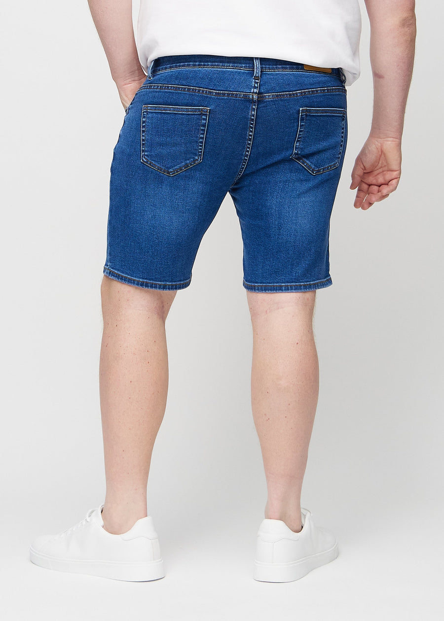 Dunkle Denim-Middle-slim-Shorts von hinten an einem Plus-Size-Model gesehen, sodass man das gesamte Produkt sehen kann.