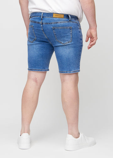 Denim middle-slim Shorts von hinten an einem Plus-Size-Model gesehen, sodass man das gesamte Produkt sehen kann.
