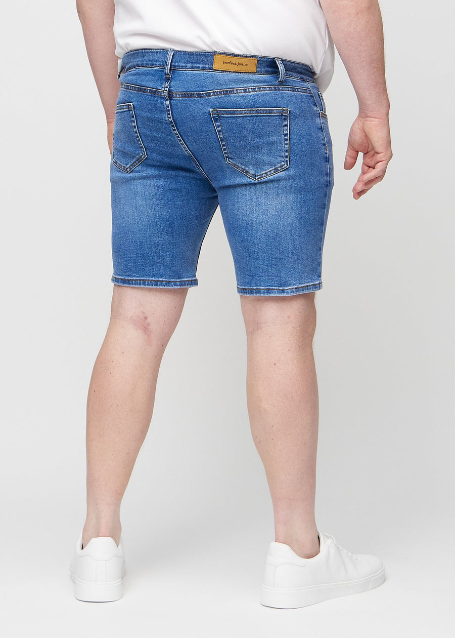 Denim middle-slim Shorts von hinten an einem Plus-Size-Model gesehen, sodass man das gesamte Produkt sehen kann.