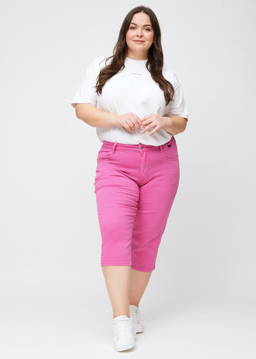 Fuldt billede af plus-size model i lyserøde slim capris.
