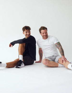 To mænd der sidder og strækker ud, iført lyse- og mørkegrå denim shorts fra Perfect Jeans.