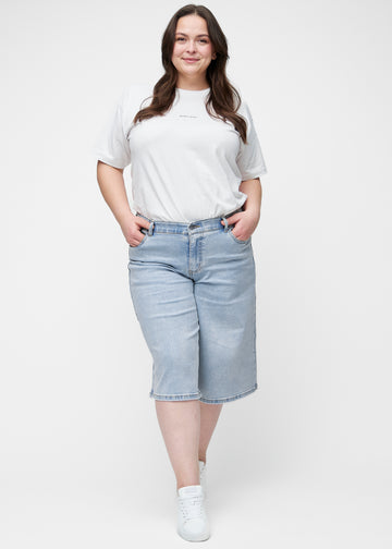 Plus-size model viser løse, lyseblå denim capris i farven Waves i bevægelse og demonstrerer pasform og materiale.