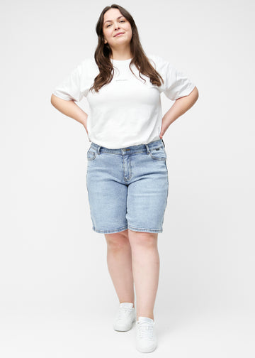 Plus-size model viser lyseblå denim shorts til kvinder i farven Waves med loose pasform i bevægelse.