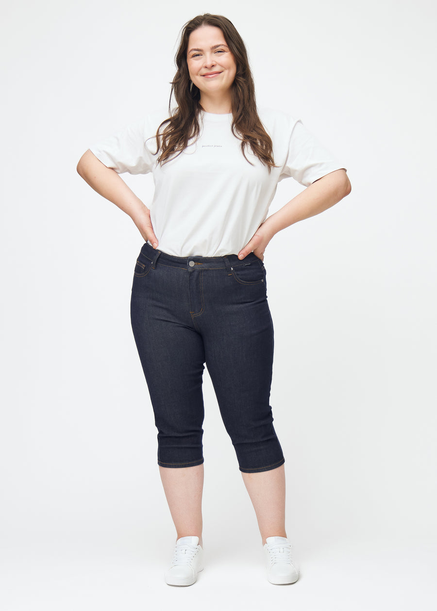 Plus-size model viser dyb mørkeblå denim capris til kvinder i farven Midnights med skinny pasform i bevægelse.