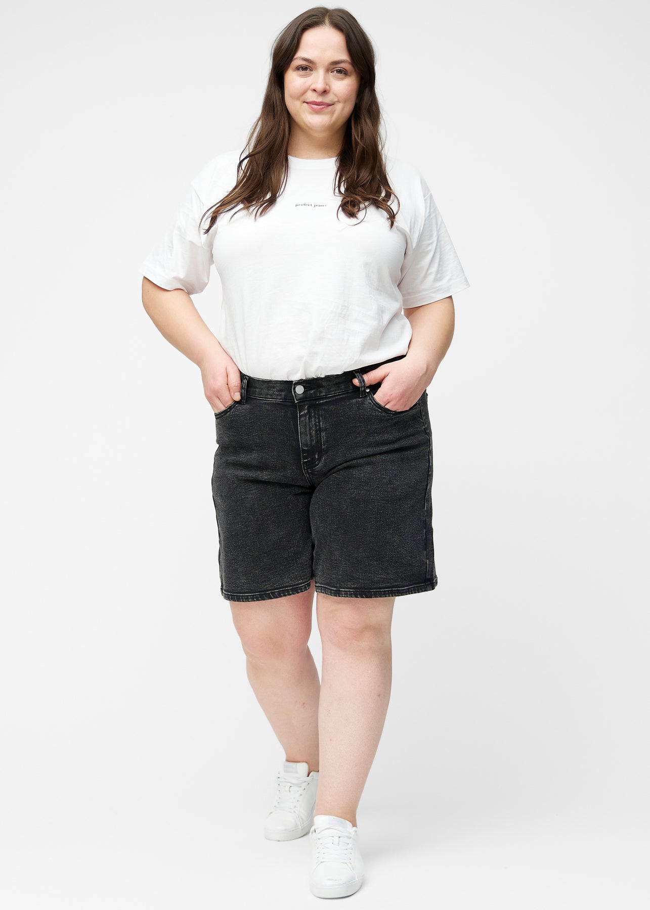 Plus-size model viser løse, mørkegrå denim shorts i farven Shadows i bevægelse og demonstrerer pasform og materiale.