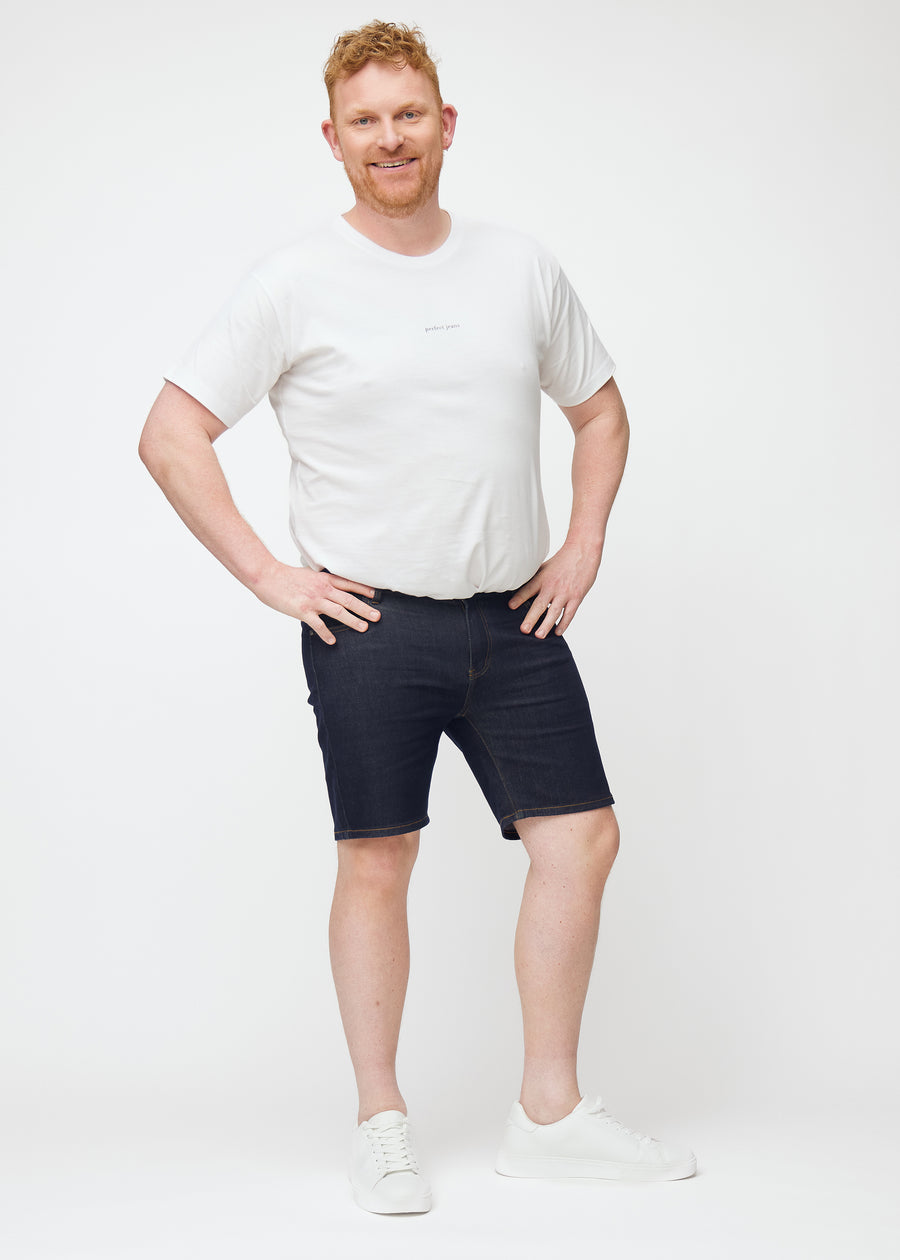 Plus-size model viser dyb mørkeblå denim shorts til mænd i farven Midnights med slim pasform i bevægelse.