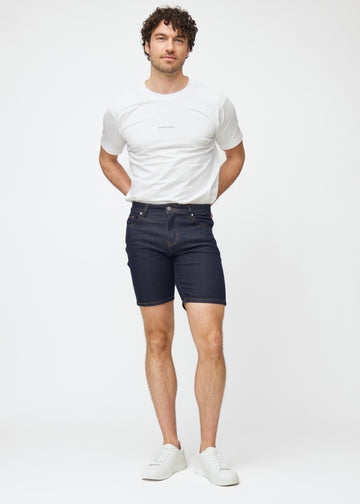 Model viser dyb mørkeblå denim shorts til mænd i farven Midnights med slim pasform i bevægelse.