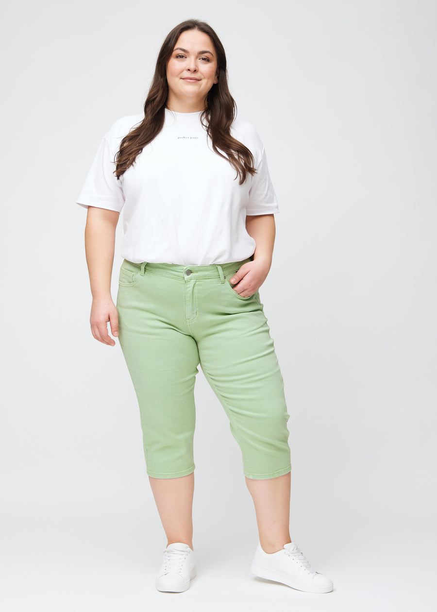 Plus-size model går ind i billedet, strækker i sine lysegrønne slim capris, drejer rundt for at vise dem frem og forlader derefter billedet.