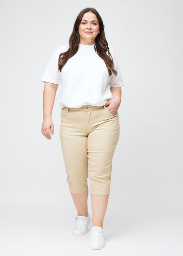  Plus-size model går ind i billedet, strækker i sine beige slim capris, drejer rundt for at vise dem frem og forlader derefter billedet.